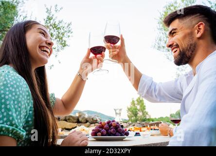 Bruna caucasica per capelli lunghi giovane donna tostando all'aperto con un attraente uomo bearded che alza al cielo bianco il loro rosso Bicchieri da vino - fritta felice Foto Stock