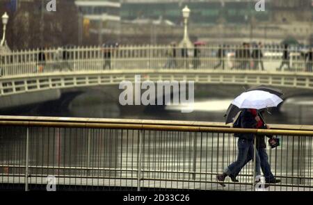 Pedoni che trasportano ombrelli che attraversano il ponte pedonale Wellington Quay sul fiume Liffey, a Dublino, Irlanda, durante una delle tante docce pesanti. Il famoso Ha'penny Bridge può essere visto sullo sfondo. Foto Stock