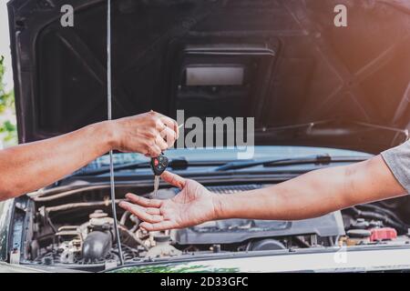 Closeup alle mani del meccanico sta restituendo le chiavi ai clienti che hanno riparato la vettura nel garage dopo che le riparazioni sono state fatte, trasp Foto Stock