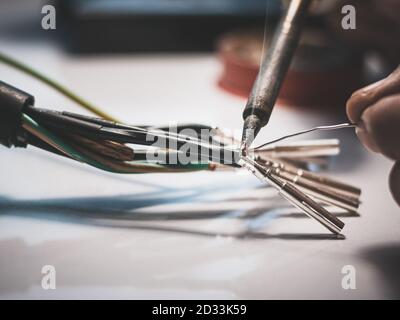 Gli elettricisti utilizzano un saldatore per collegare i fili al pin metallico con un cavo di saldatura. Foto Stock