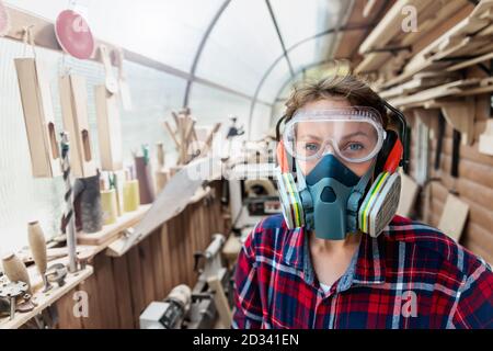 Giovane adulto caucasico medio invecchiato professionale falegname femmina macinazione legno grezzo con levigatrice orbitale utensile in Falegnameria fai da te officina. Donne femminili Foto Stock