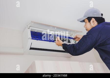 L'addetto alla riparazione dell'aria condizionata nell'uniforme blu sta rimuovendo il filtro dell'aria per la pulizia. Foto Stock