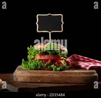 cheeseburger con carne tritata, lattuga verde e ketchup su una tavola di legno marrone cucina, un segno di legno si stacca nel sandwich Foto Stock