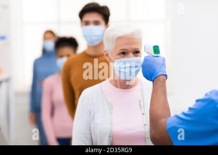 Lavoratore medico che fa lo screening della temperatura per Senior Woman Indoor Foto Stock