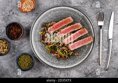 bistecche di tonno alla griglia su un piatto moderno con un'insalata di funghi, verdure e semi di sesamo, vista dall'alto Foto Stock