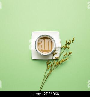 Tazza di caffè con fiori secchi blu misty su sfondo verde. Vista dall'alto, spazio copia Foto Stock