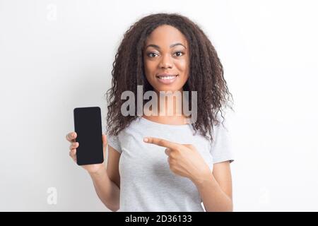 La donna afroamericana mostra il dito sullo schermo vuoto dello smartphone. Foto Stock