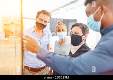 Uomini d'affari in riunione d'affari con la maschera facciale nel ufficio a causa del coronavirus e Covid-19 Foto Stock