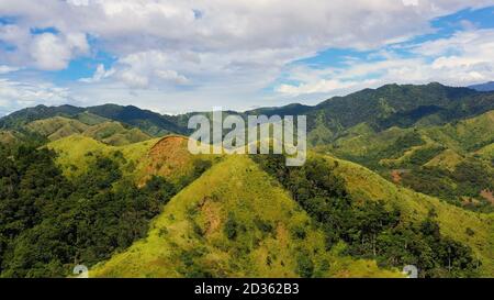 Montagne e colline con foresta pluviale ed erba verde sotto un cielo blu con nuvole su una soleggiata giornata estiva. Filippine, Luzon. Paesaggio estivo. Foto Stock