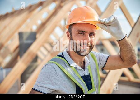 Uomo che lavora sodo che ribalta il suo casco protettivo in cantiere Foto Stock