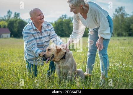 felice coppia senior giocare con labrador retriever cane in sole parco estivo Foto Stock