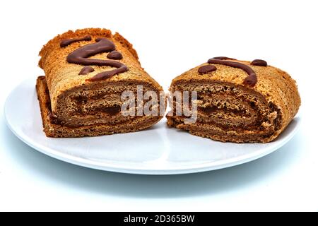 Rotolo di cioccolato fatto in casa su piatto, isolato su sfondo bianco. Pasticcini fatti a mano cosparsi di cacao. Delizioso rotolo coperto di cioccolato. Foto Stock