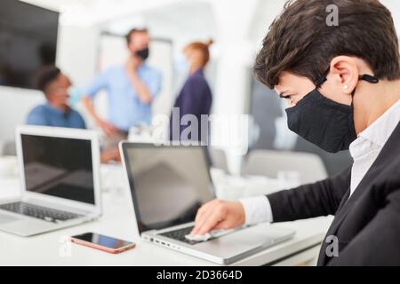 Uomo d'affari con maschera quotidiana disinfettare il suo computer a causa di Covid-19 Foto Stock