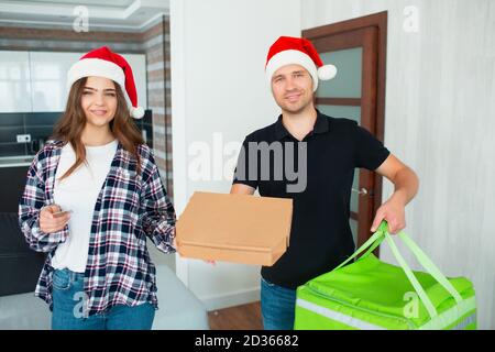 buon natale e Felice Anno Nuovo. L'uomo di consegna del cibo in cappello rosso di santa ha portato ordine alla donna. Entrambi guardano la macchina fotografica e truffano Foto Stock