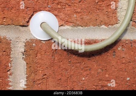 Cavo coassiale e ordinato con foro in plastica bianca in una struttura muro di mattoni Foto Stock