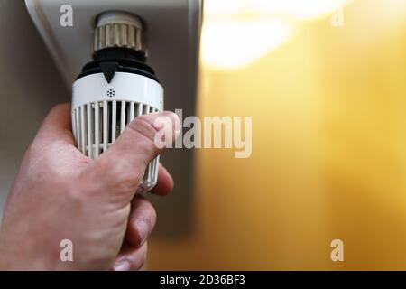Mano dell'uomo che regola la valvola del termostato del radiatore sull'icona del ghiaccio fiocco di neve, simbolo per risparmiare denaro a costi di riscaldamento o a basse temperature, primo piano. Foto Stock