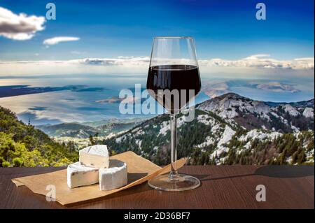 Bicchiere o vino rosso con formaggio brie contro la bella montagna paesaggio con vista mare blu e pini in Croazia Foto Stock