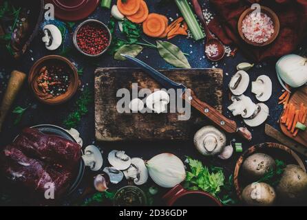 Verdure biologiche fresche, ingredienti, spezie e carne per zuppa o brodo su sfondo tavola da cucina vintage con tagliere in legno rustico. Via superiore Foto Stock