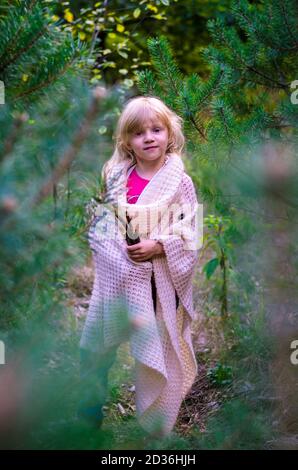 adorabile ragazza bionda sola tra alberi di pino verde in autunnale legno Foto Stock