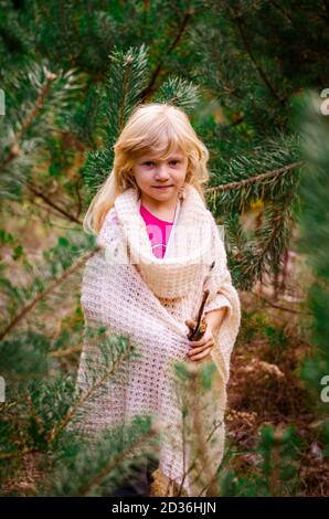 adorabile ragazza bionda sola tra alberi di pino verde in autunnale legno Foto Stock