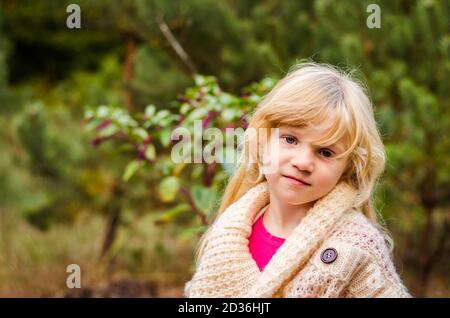 adorabile ragazza bionda sola tra alberi di pino verde in autunnale legno Foto Stock