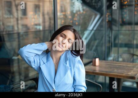 Dolore al collo. Closeup ritratto stressato infelice donna di affari con mal di collo cattivo malattia, dopo lunghe ore di lavoro o di studio seduto sulla terrazza bar b Foto Stock