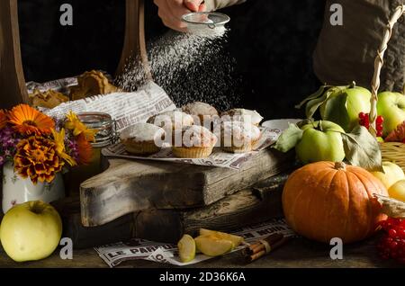 Donna cospargere lo zucchero a velo su deliziosi muffin fatti in casa di mela e zucca su sfondo scuro, cottura di Halloween Foto Stock