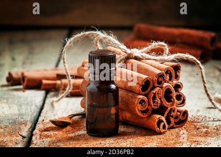 Olio essenziale di cannella in una piccola bottiglia, cannella macinata e bastoncini di cannella su vecchio sfondo di legno, fuoco selettivo Foto Stock