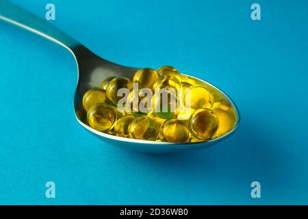 Cumulo di capsule rotonde di olio di pesce in cucchiaio metallico su sfondo blu, fuoco selettivo, primo piano Foto Stock