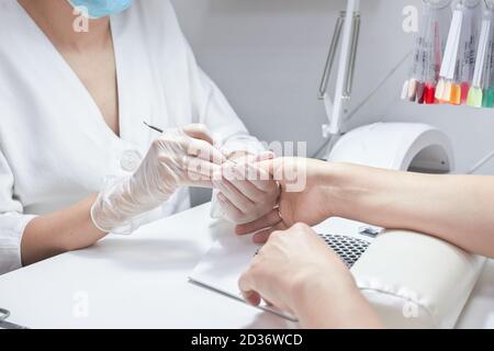 manicure professionale che spinge la cuticola sulla mano femminile con spintore. primo piano del processo di manicure a mano. cura del salone e della spa per mani e unghie. tavolozza dei colori delle lucidanti in gel. Foto Stock