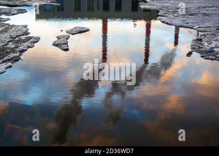 Riflessione in puddle di tre camini fumo. Tubi industriali. Concetto di inquinamento atmosferico Foto Stock