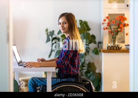 Giovane donna in sedia a rotelle che usa il computer portatile a casa Foto Stock