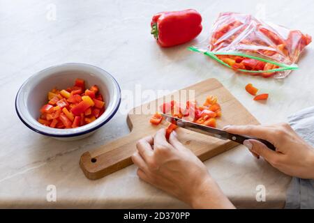 le mani della donna tagliano peperoni freschi e li mettono dentro un sacchetto congelatore Foto Stock