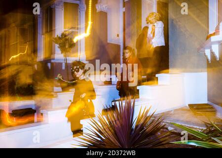 Tre giovani donne trick-or-treaters in costumi di Halloween lasciando una casa essendo stati dati di dolci e altre ricompense, Londra, Regno Unito Foto Stock