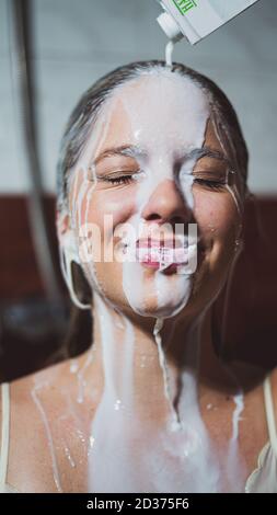 Colpo verticale di una bella giovane donna che ha versato il latte sopra la testa per un bagno di latte Foto Stock