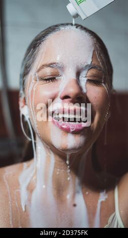 Colpo verticale di una bella giovane donna che ha versato il latte sopra la testa per un bagno di latte Foto Stock