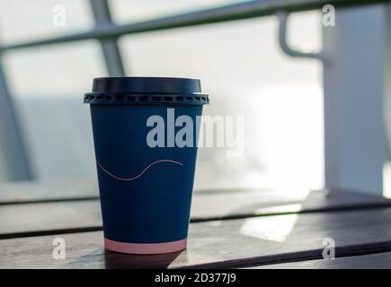 Tazza da caffè di carta monouso blu scuro con coperchio in plastica nera su tavolo di legno alla nave da crociera Foto Stock