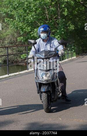 Un uomo di mezza età su una motocicletta di Pace & che indossa una maschera gira intorno al lago in Kissena Park, Flushing, New York.