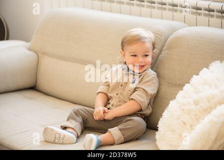 Bel ragazzo vestito e felice con gli occhi blu seduti sul divano. Foto Stock