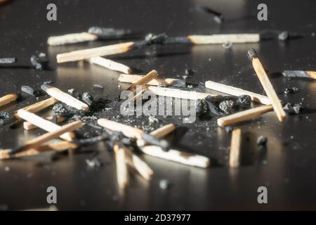 Usato fiammiferi di legno con i resti di ceneri su una tavola nera. Messa a fuoco selettiva. Contrasto elevato. Foto Stock