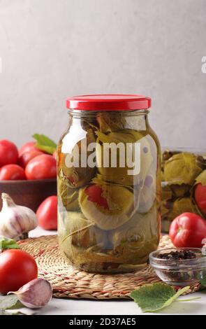 Pomodori marinati con aglio in foglie d'uva in due vasetti di vetro su sfondo grigio. Primo piano. Foto Stock