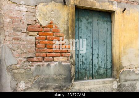 Porta di legno verde pallido in un muro di mattoni rossi dilapidato E gesso giallo e marrone in una casa in Italia Foto Stock