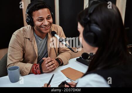 Portait di felice conduttore di radio maschile sorridente, parlando con ospite femminile mentre moderando uno spettacolo dal vivo in studio Foto Stock