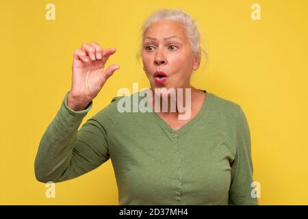 Donna anziana sorpresa mostra qualcosa di piccolo con le mani Foto Stock