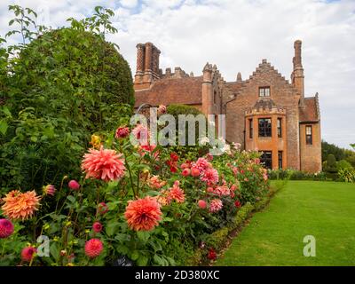 Chenies Manor giardini nel mese di settembre. Splendida pesca e salmone rosa Dahlia mostra con il Tudor Manor come sfondo in un bel pomeriggio in tarda estate. Foto Stock