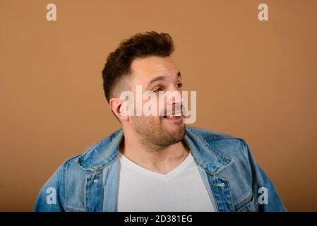 Bell'uomo in piedi e sorridente isolato sullo sfondo marrone chiaro dello studio. Foto Stock