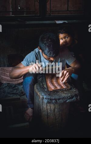 Dalit lavora al buio con sua figlia che lo guarda. Un gruppo di giovani lavora in un piccolo edificio in un sobborgo di Kathmandu, Nepal. Foto Stock