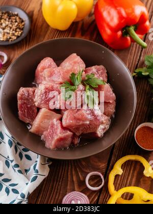 kebab di maiale fresco crudo marinato in una ciotola con verdure sullo sfondo Foto Stock