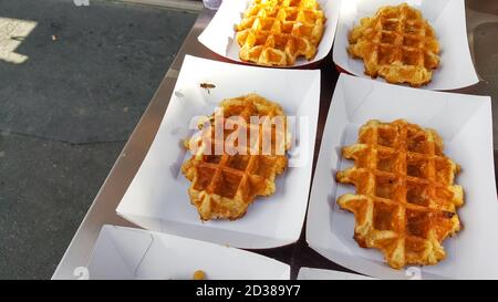 Le api volano e atterrano su waffle belgi all'aperto Un fornitore di cibo di strada a Parigi, Francia Foto Stock