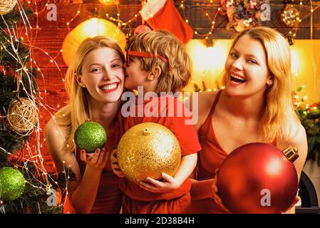 Ragazze belle giovani e capretto piccolo dal tree.Ready di Natale al partito. Decorazione di Natale. Il ragazzino sta baciando la sorella. Foto Stock